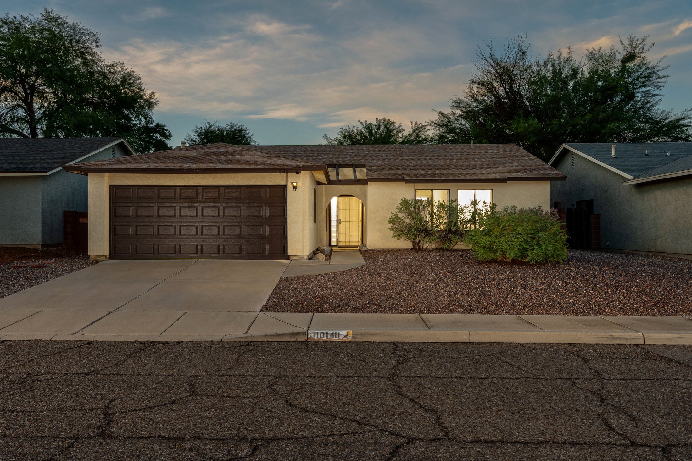 Twilight curb view with porch light and house number 10140.