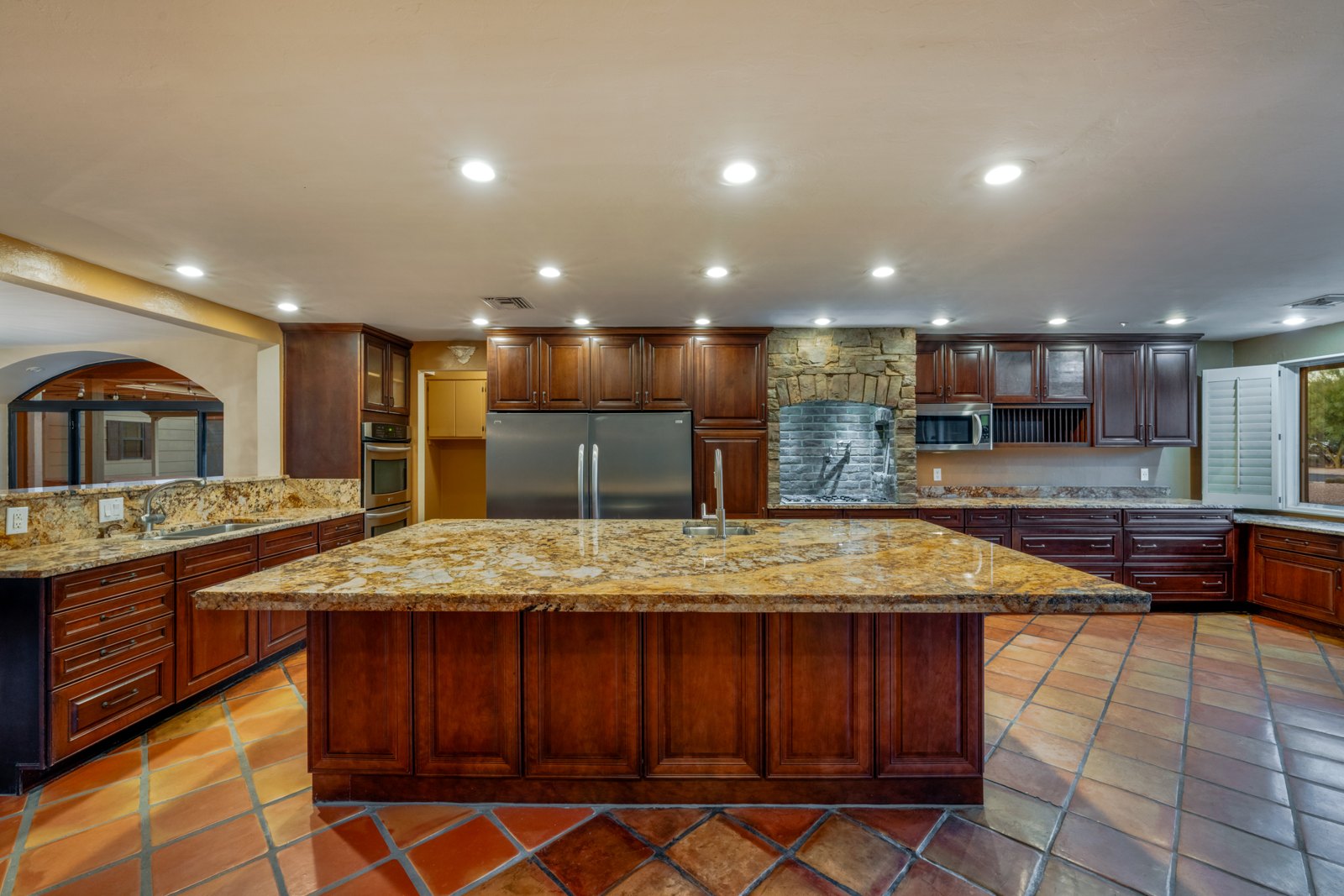 Island kitchen with dark wood cabinets, double wall ovens and a pot filler